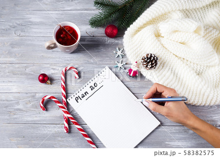 Hand of woman writing on notepad Christmas greetings with tea, decoration on wooden background 58382575