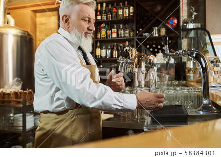 Barman standing at bar counter pouring beer in glass. Barman standing at bar counter pouring beer in glass. 58384301