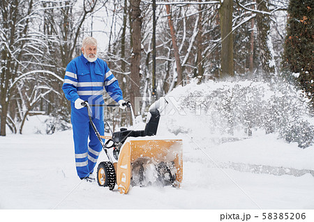 Man working with snowblower and removing snow from footpath 58385206