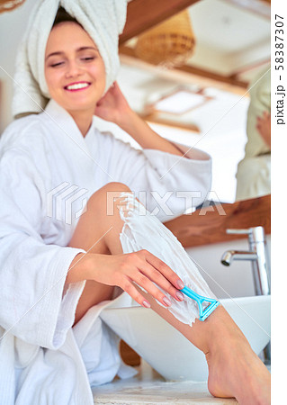 Photo of happy woman in white coat shaving her legs in bath Photo of happy woman in white coat shaving her legs in bath 58387307