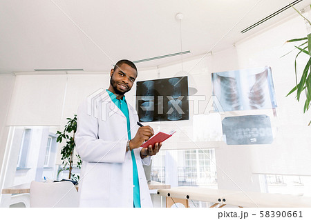 health and medicine concept - smiling African man doctor studying x-ray of the patients while health and medicine concept - smiling African man doctor studying x-ray of the patients while 58390661