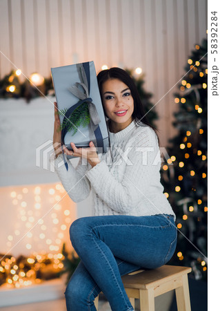 Happy girl in excitement opening Christmas box trying to guess what is inside. Excited woman Happy girl in excitement opening Christmas box trying to guess what is inside. Excited woman 58392284