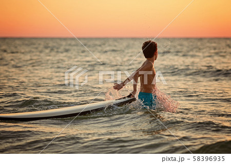 Happy little surfer boy makes splashes with hands at golden sunset 58396935