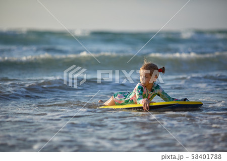 Little baby girl young surfer with bodyboard has a fun on small ocean waves. Active family lifestyle 58401788