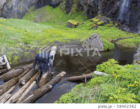 man hiker standing on wooden log takeing up clean water, filling 58402562