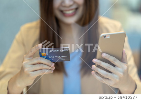 Closeup Asian woman using credit card with mobile for online shopping in department store over the clothes shop store background, technology money wallet and online payment concept, credit card mockup Closeup Asian woman using credit card with mobile for online shopping in department store over the clothes shop store background, technology money wallet and online payment concept, credit card mockup 58410577