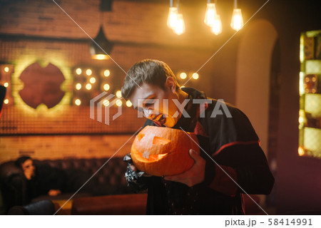 Young man in a Halloween costume of Count Dracula holds a carved festive pumpkin 58414991