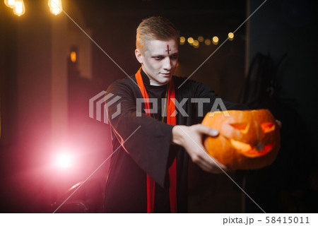 Young man in a Halloween costume holding a carved pumpkin on his outstretched arm Young man in a Halloween costume holding a carved pumpkin on his outstretched arm 58415011