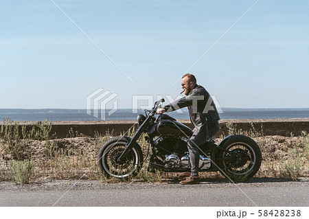 Brutal athletic biker sitting on the motorcycle by the ocean Brutal athletic biker sitting on the motorcycle by the ocean 58428238