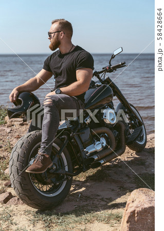 Handsome muscular man sitting on his motorcycle looking at the sea Handsome muscular man sitting on his motorcycle looking at the sea 58428664