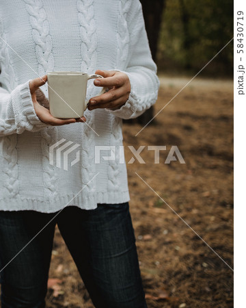 young woman in a white sweater holds a cup of tea 58430719