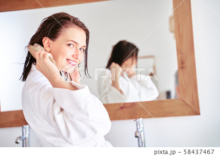 Photo of brunette woman combing her hair in front of bathroom mirror . Photo of brunette woman combing her hair in front of bathroom mirror . 58437467