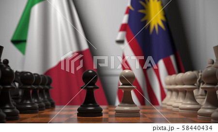 Flags of Italy and Malaysia behind pawns on the chessboard. Chess game or political rivalry related 58440434