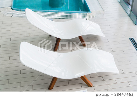 Empty two white lounge chairs inside of tiled room near swimming pool. Nobody in spa room. Deck Empty two white lounge chairs inside of tiled room near swimming pool. Nobody in spa room. Deck 58447462