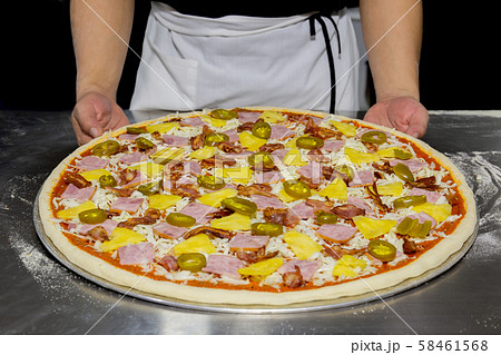 Chefs hand with hawaiian pizza and pineapple, pickled chilli ,ham on the table. 58461568
