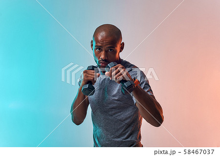 Work hard Muscular young african man exercising with dumbbells while standing against colorful Work hard Muscular young african man exercising with dumbbells while standing against colorful 58467037