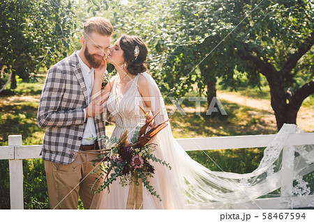 Caucasian couple in love bride and groom standing in embrace near wooden white, rural fence in park 58467594