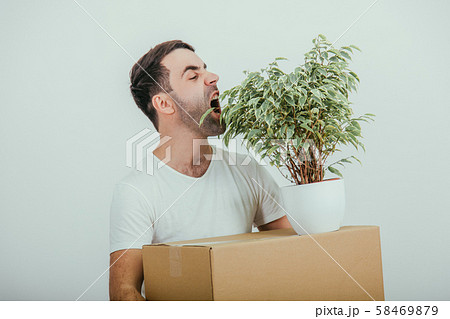 Funny young man moving into new house, standing, holding carton box and flowerpot, pretending that Funny young man moving into new house, standing, holding carton box and flowerpot, pretending that 58469879