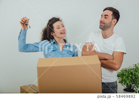 Young wife and husband standing behind the big carton box, together. Woman is holding keys to their Young wife and husband standing behind the big carton box, together. Woman is holding keys to their 58469892