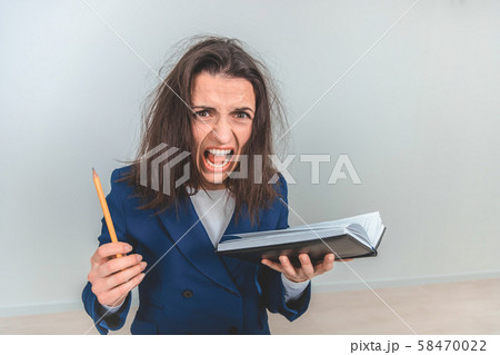 Exhausted young teacher with tousled hair holdingnotebook and pen, leaning to the camera, screaming Exhausted young teacher with tousled hair holdingnotebook and pen, leaning to the camera, screaming 58470022