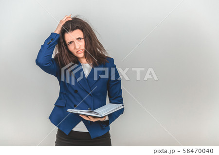 Upset female teacher standing with notebook in hands, keeping hand on the head, looking tired Upset female teacher standing with notebook in hands, keeping hand on the head, looking tired 58470040
