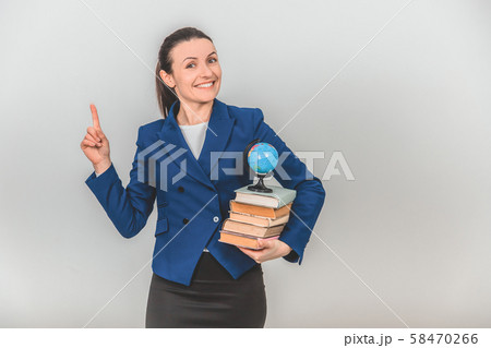 Happy female teacher holding a stack of colorful books, pointing her finger up, calling to pay 58470266