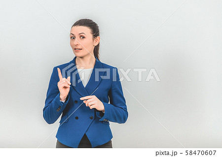 Serious young teacher standing, raising her finger up, calling to pay attention to something Serious young teacher standing, raising her finger up, calling to pay attention to something 58470607