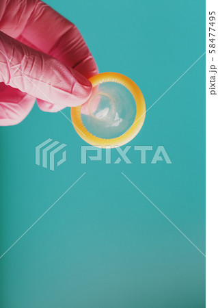 An opened condom in a hand in a pink glove holds An opened condom in a hand in a pink glove holds 58477495