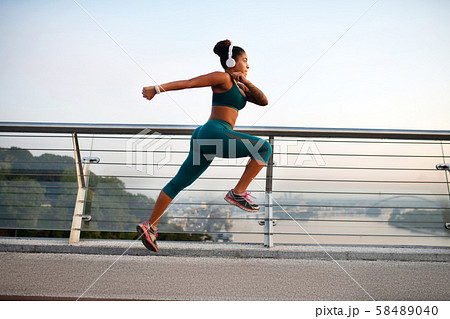 Dark-skinned woman wearing white earphones running fast 58489040