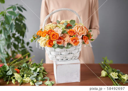 Florist woman creates flower arrangement in a wicker basket. Beautiful bouquet of mixed flowers Florist woman creates flower arrangement in a wicker basket. Beautiful bouquet of mixed flowers 58492697