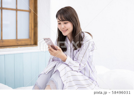 スマホを見る女性 寝室 ベッド パジャマ スマホを見る女性 寝室 ベッド パジャマ 58496031