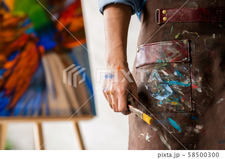 Part of professional painter in dirty apron holding paintbrush in hand 58500300