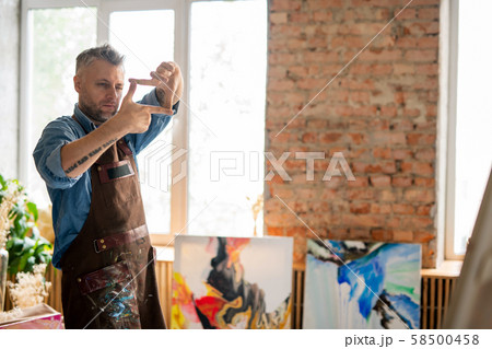 Professional painter looking at easel through frame made up of fingers 58500458