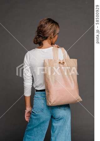 Back view of young female in casualwear holding nude beige tote bag on shoulder 58500929