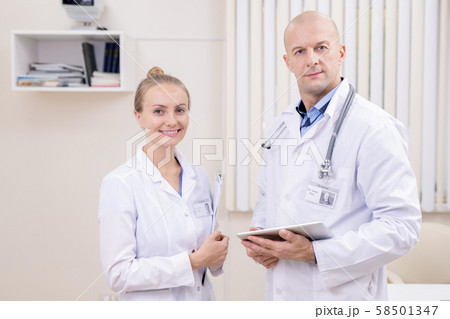 Happy young successful clinician and her bald serious colleague in whitecoats Happy young successful clinician and her bald serious colleague in whitecoats 58501347