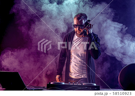 Trendy male dj posing against mixing console Trendy male dj posing against mixing console 58510923