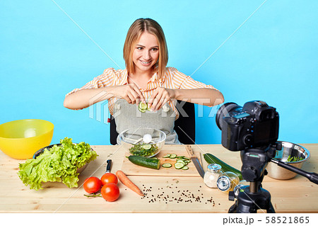 Female chef sits at table with products, makes healthy salad with vegetables Female chef sits at table with products, makes healthy salad with vegetables 58521865
