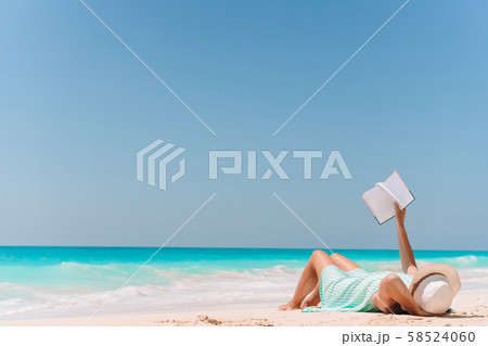 Young woman reading book on chaise-lounge on the beach Young woman reading book on chaise-lounge on the beach 58524060