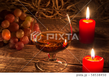 glass with brandy or cognac, grapes and candle on aged wood table background. Close-up view. 58538450
