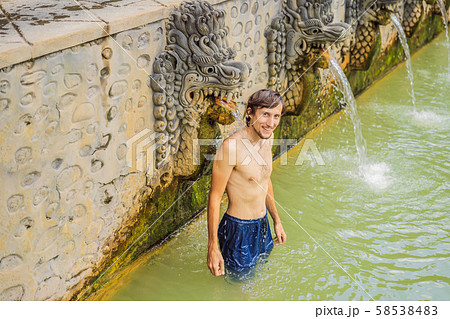 Young man in hot springs banjar. Thermal water is released from the mouth of statues at a hot 58538483
