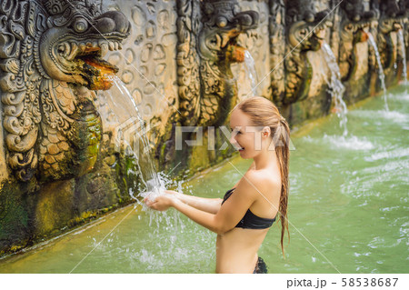 Young woman in hot springs banjar. Thermal water is released from the mouth of statues at a hot 58538687