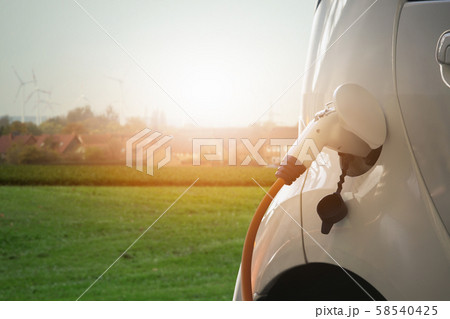 Close up of electric car with a connected charging cable on the blurred background of a city using renewable energy Close up of electric car with a connected charging cable on the blurred background of a city using renewable energy 58540425