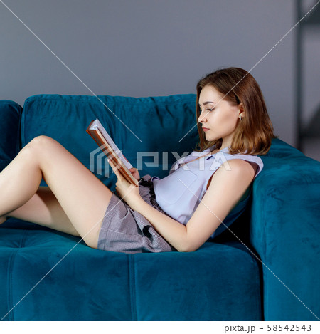 Young woman sits on the couch and looks in her diary. Young woman sits on the couch and looks in her diary. 58542543