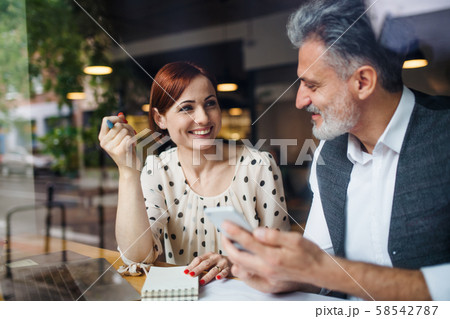 Man and woman having business meeting in a cafe, using smartphone. 58542787