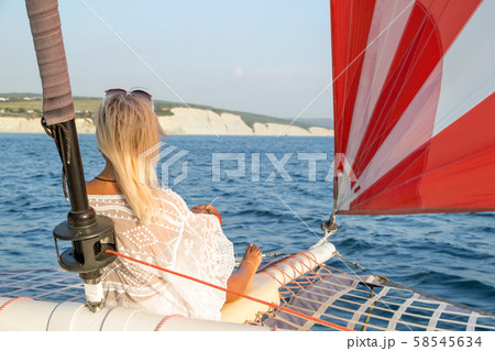 Beautiful young fair-haired woman dressed in a swimsuit and white pareo sitting on a yacht bow Beautiful young fair-haired woman dressed in a swimsuit and white pareo sitting on a yacht bow 58545634