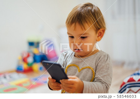 Baby using phone, playing game or watching cartoons. Home indoors. Screen time Baby using phone, playing game or watching cartoons. Home indoors. Screen time 58546033