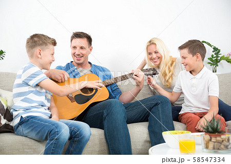 Happy caucasian family smiling, playing guitar and singing songs together at cosy modern home Happy caucasian family smiling, playing guitar and singing songs together at cosy modern home 58547334