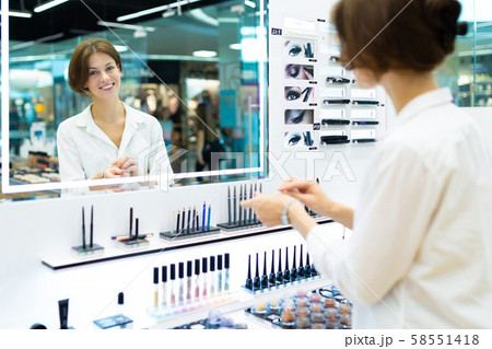 Young smiling woman in cosmetics shop is testing cosmetics in front of mirror 58551418
