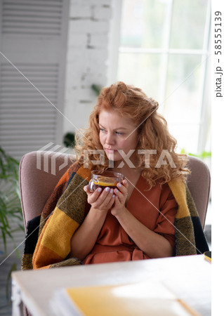 Woman with plaid on shoulders drinking tea while having cough 58555139
