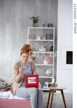 Red-haired woman taking thermometer out of first aid kit 58555217